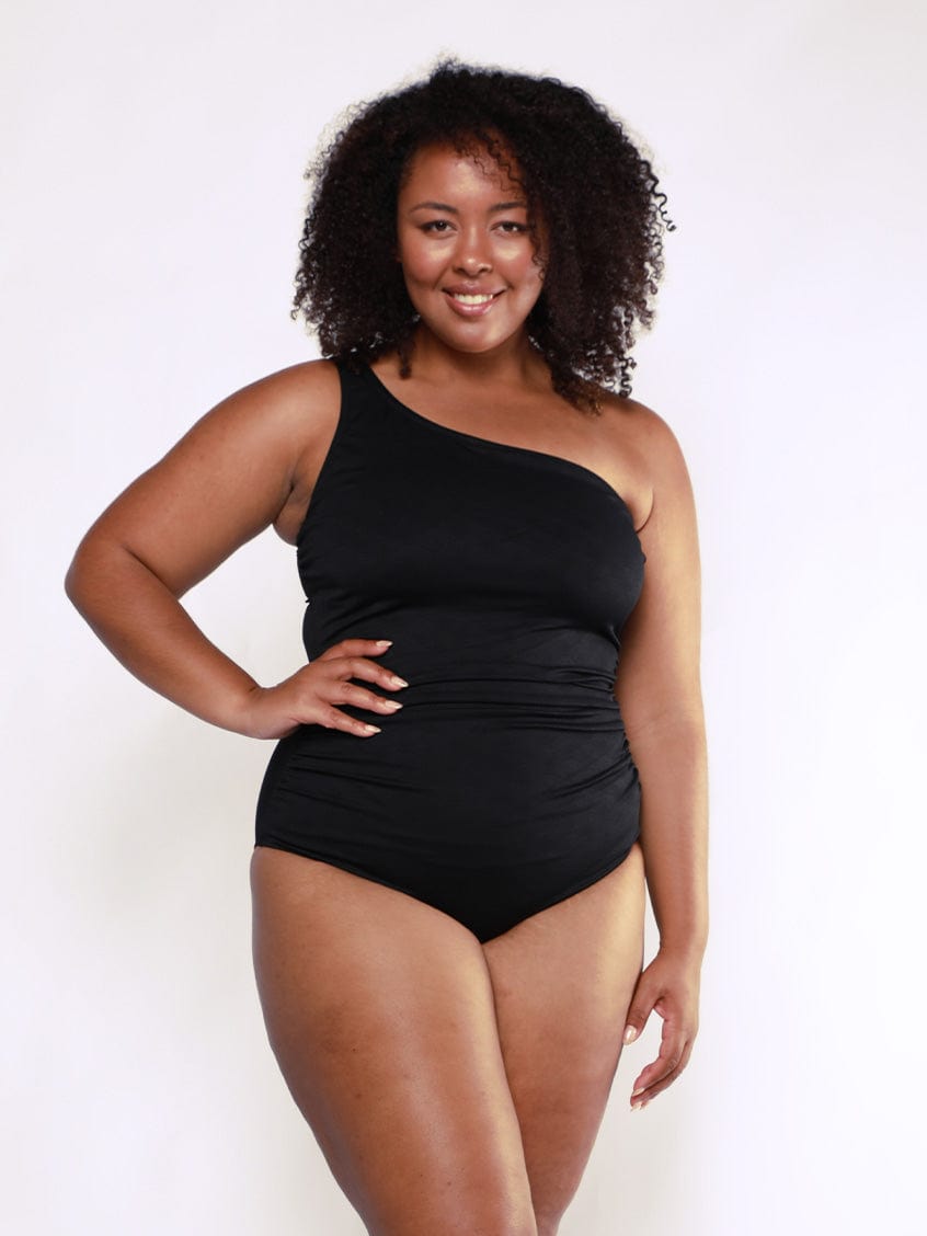 Woman wearing a black one-shoulder swimsuit against a white background