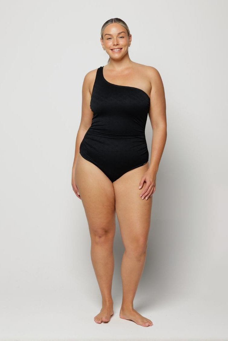 Woman wearing a black one-shoulder swimsuit on a white background