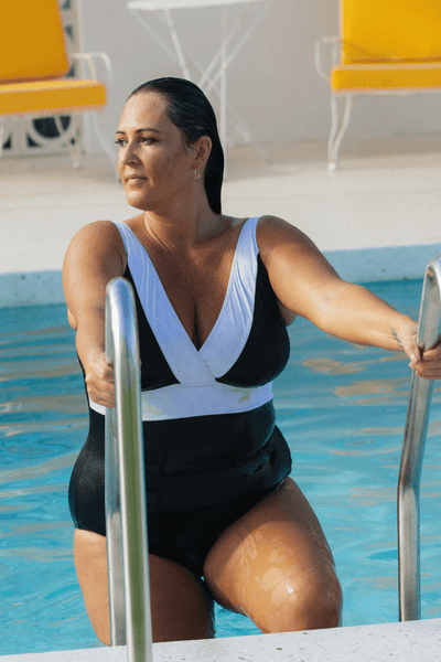 model using the step ladder to come out of the pool wearing a black v neck one piece with white trim