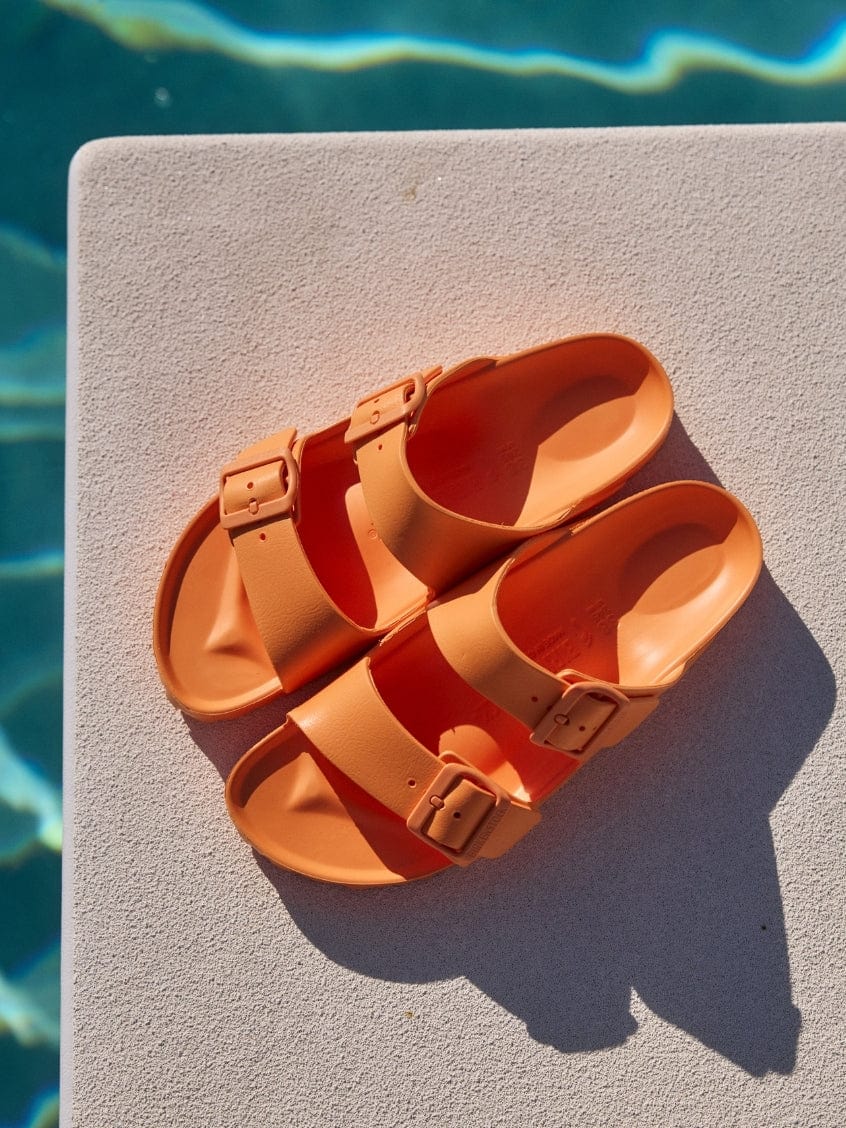 Pair of orange sandals on a diving board with water in the background