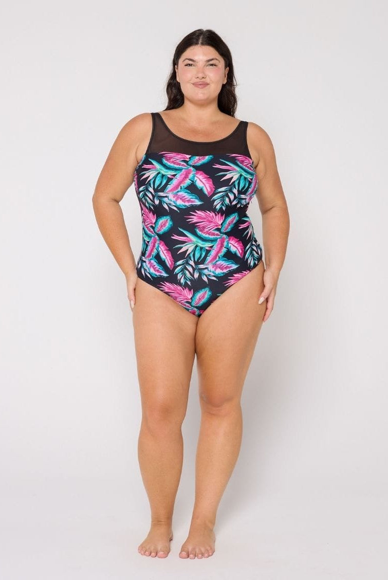 Woman wearing a black swimsuit with pink and green leaf pattern on a white background