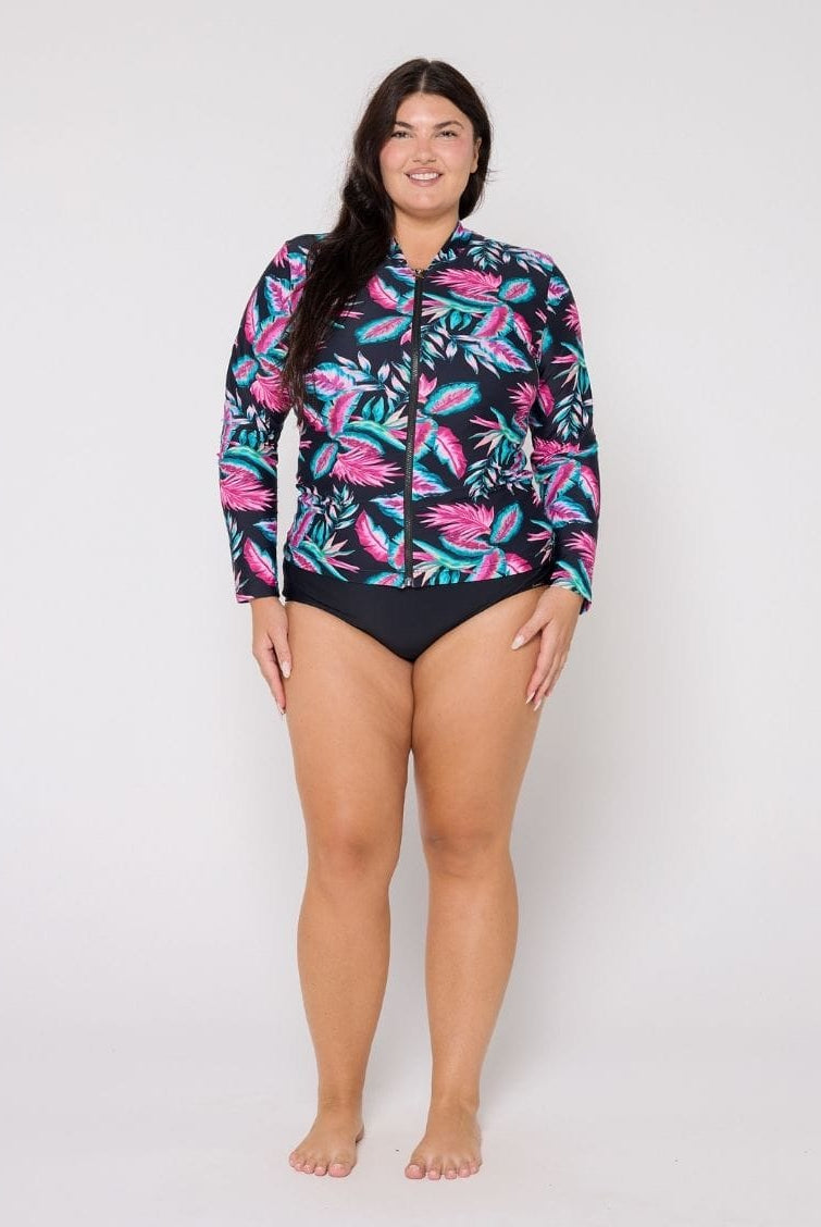 Woman wearing a colorful tropical leaf patterned rash guard on a white background