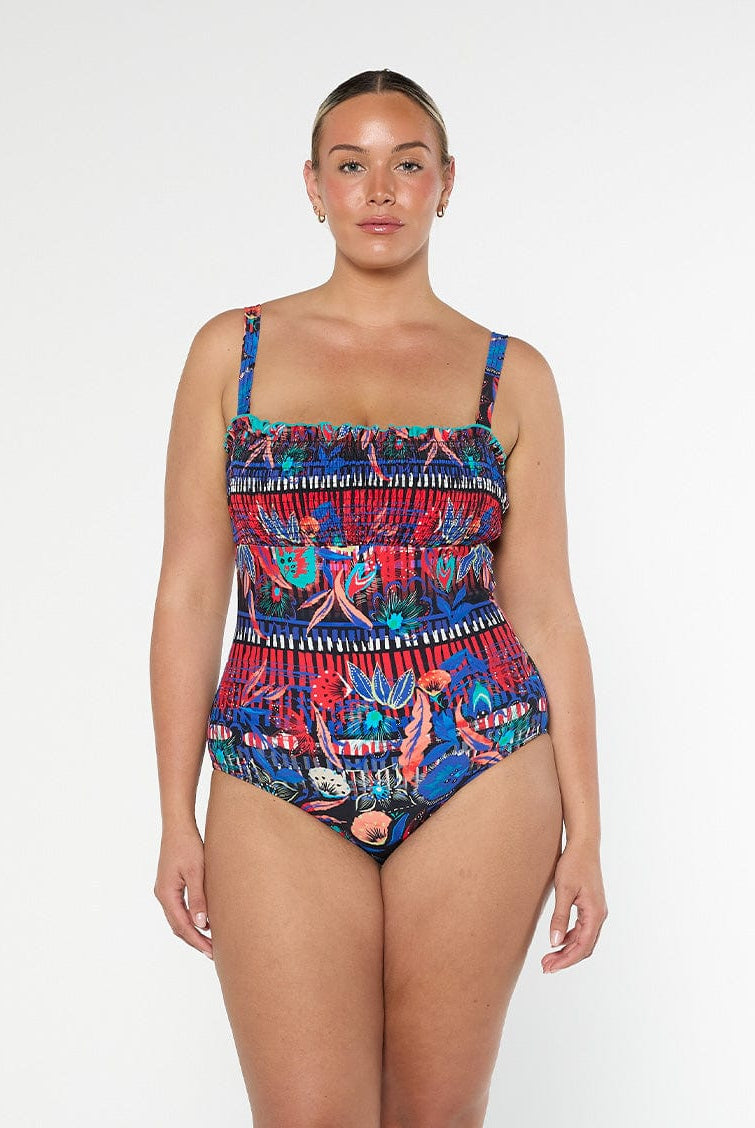 Blonde woman wearing a colorful patterned swimsuit in a studio with removable straps