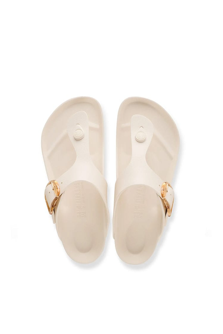 A pair of Birkenstock Thalia slide sandals in cream-colored foam with gold-tone buckle details, shown from a top-down view on a white background.