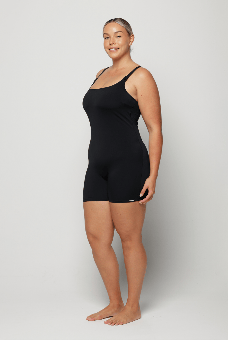 Woman wearing a black boyleg swimsuit against a white background