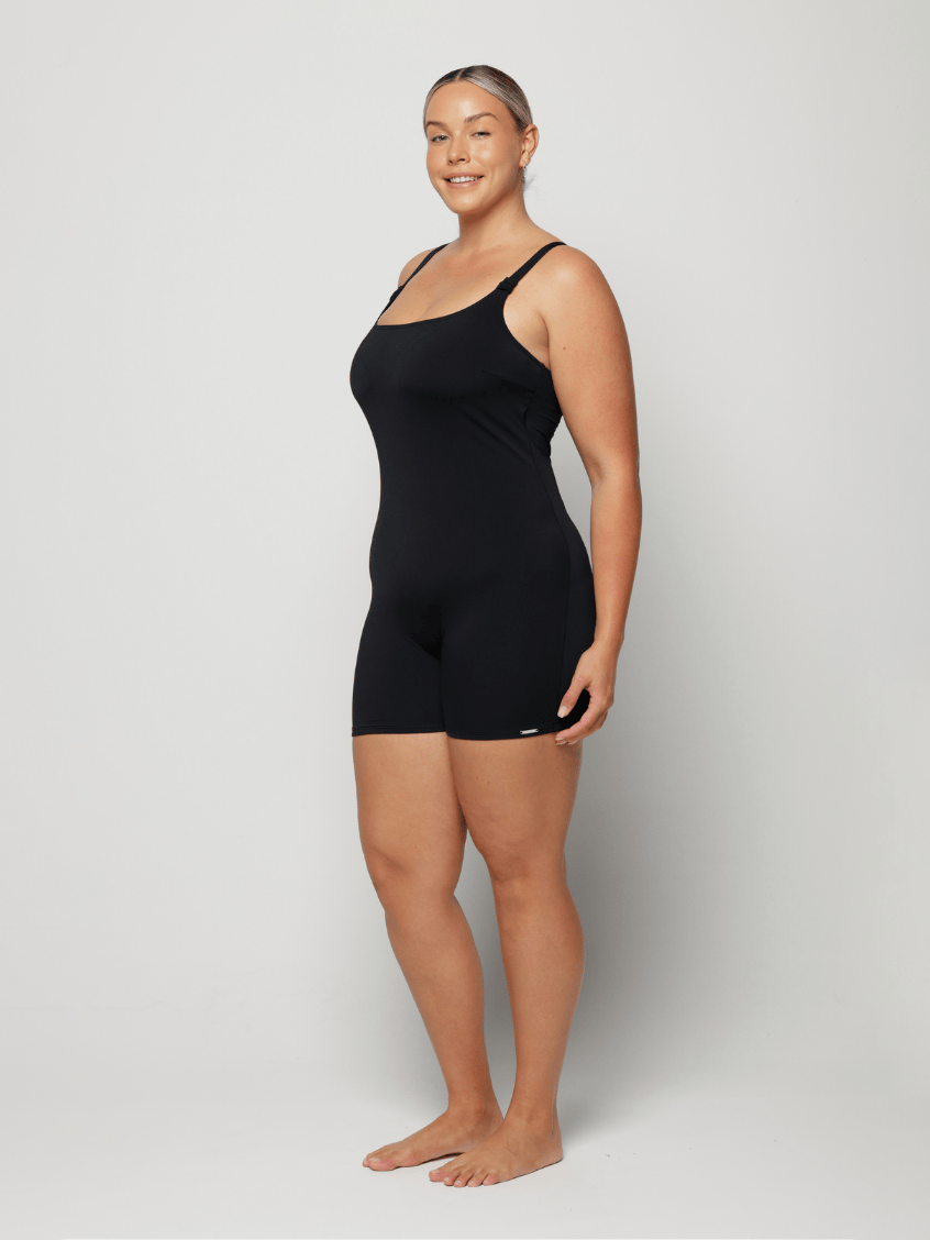 Woman wearing a black boyleg swimsuit against a white background