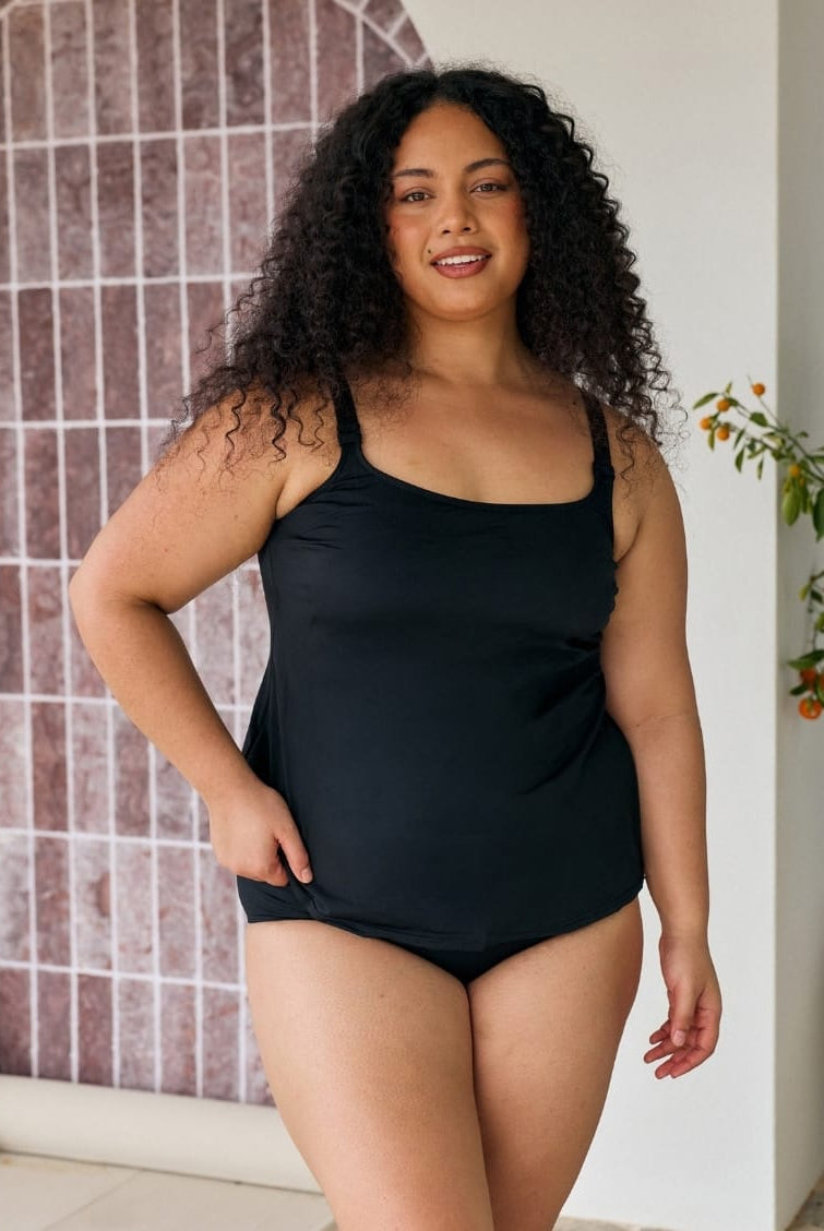 Dark hair model wearing a black chlorine resistant tank tankini top with adjustable straps