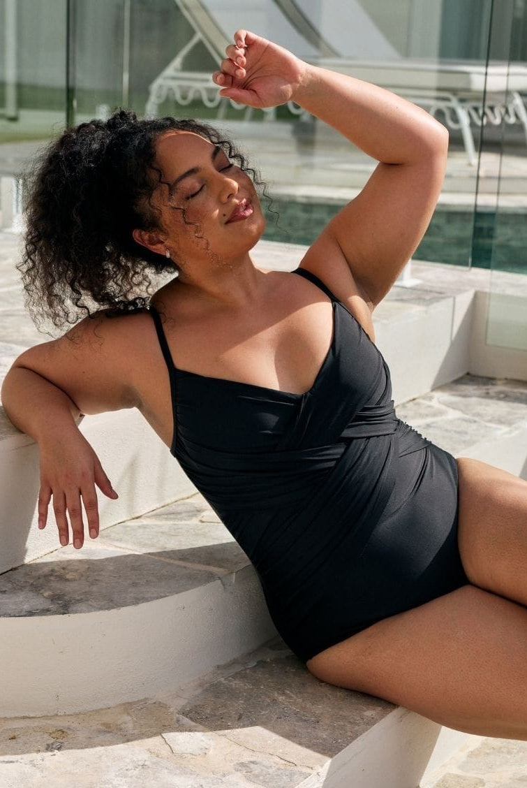Brunette model wearing a black criss cross one piece for plus size women in black metallic fabric