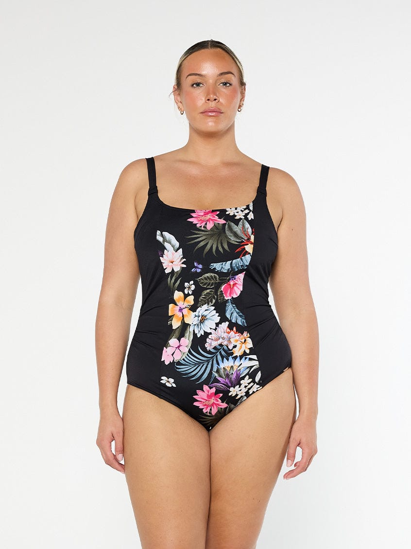 Blonde model shows front of plus size black floral one piece in chlorine resistant fabric