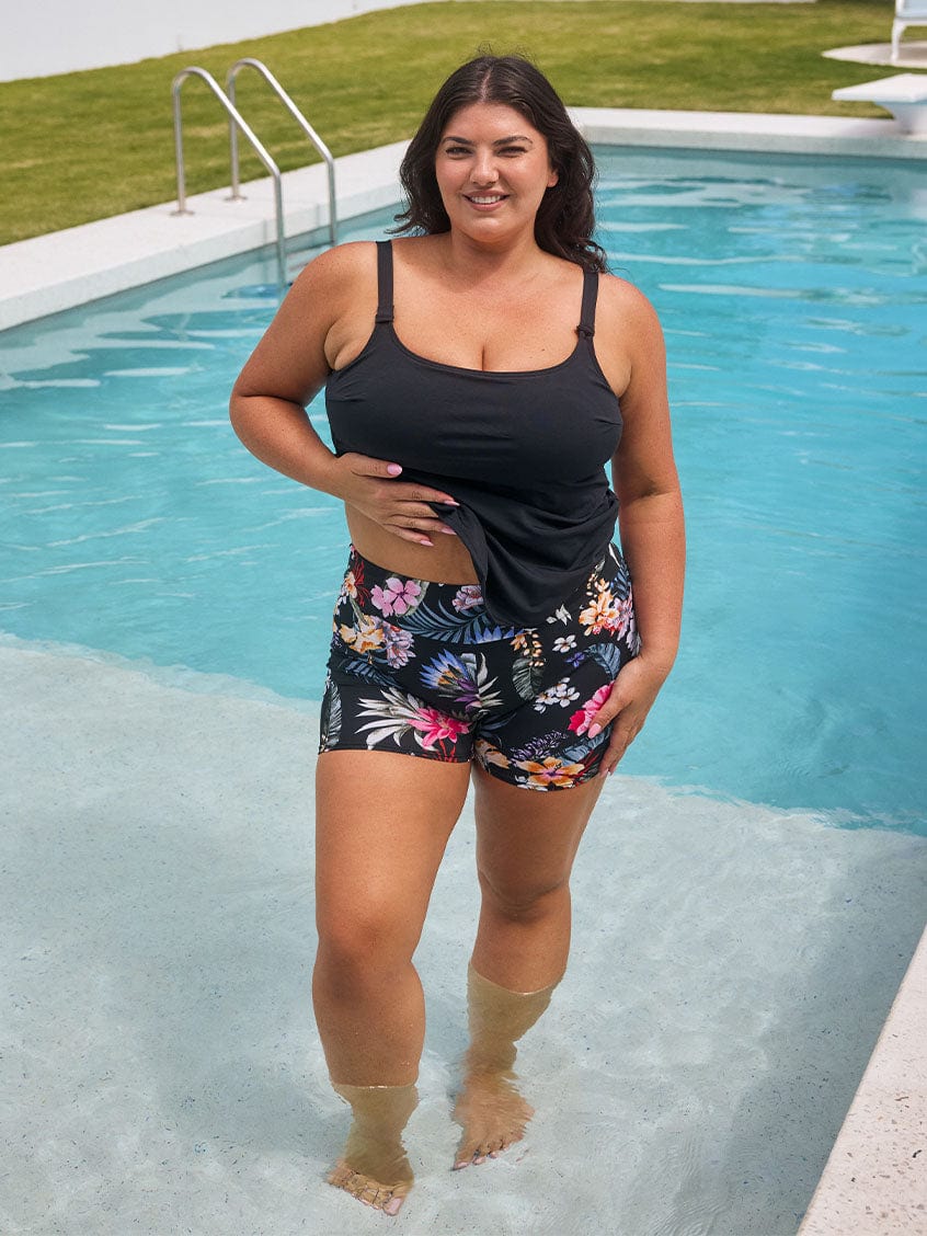 Brunette model wears high-waisted black floral chlorine resistant swim shorts