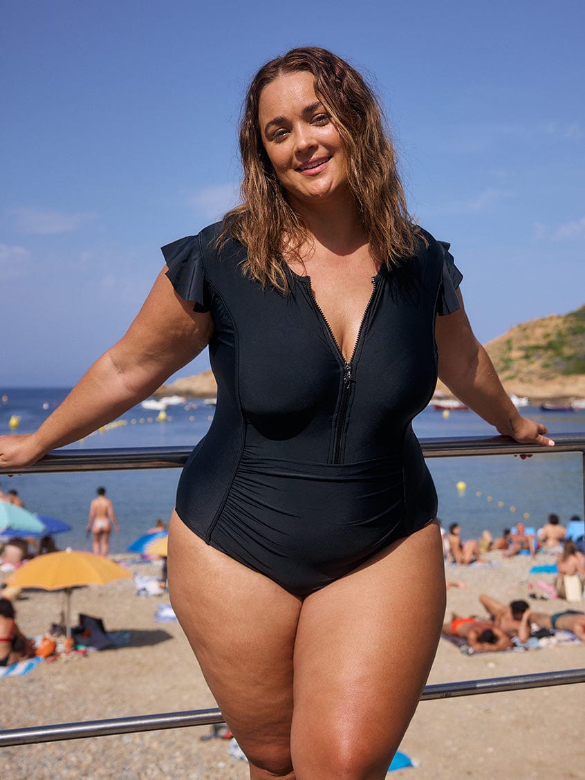 brunette curve model wearing black frill sleeve zip up one piece swimsuit