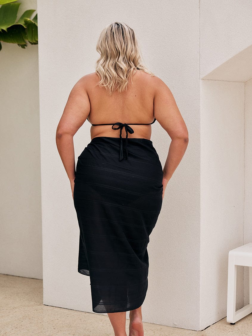 Back of model wearing black cotton sarong for curve women with pom pom detail