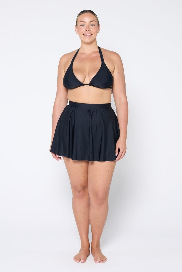 Woman wearing a black bikini set with a matching skirt on a white background