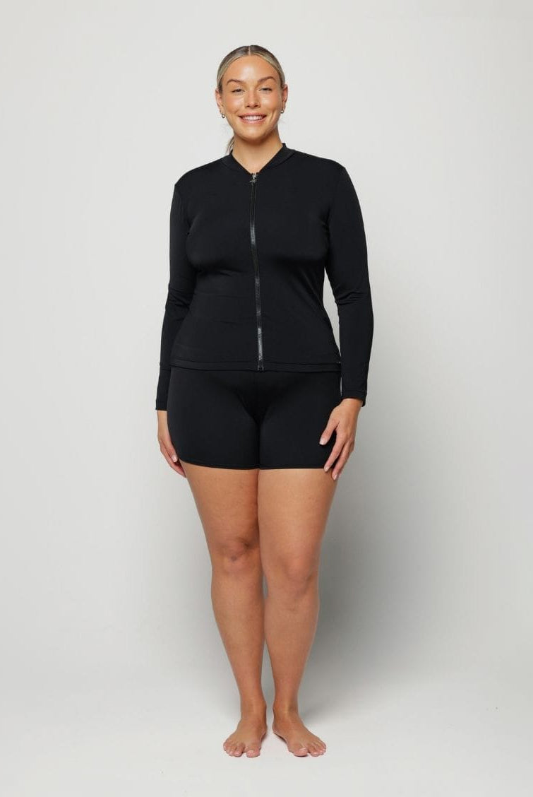 Woman wearing a black long-sleeve rash vest top with a zip and white background behind her