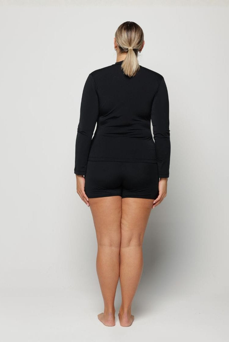 Woman wearing a black long-sleeve rash vest top with a zip and white background behind her