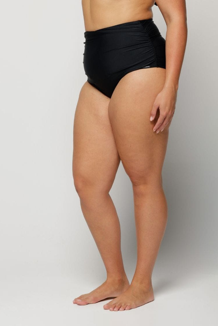 Woman wearing black high-waisted bikini bottoms on a plain background