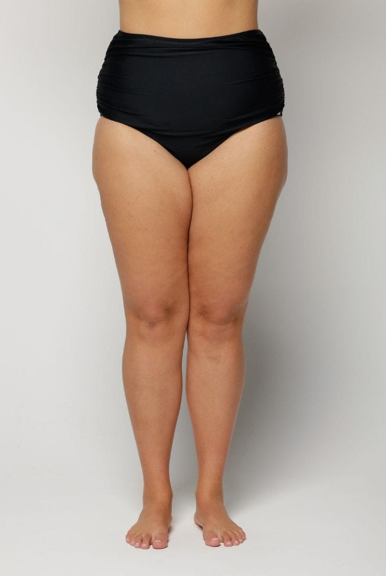 Woman wearing black high-waisted bikini bottoms on a plain background