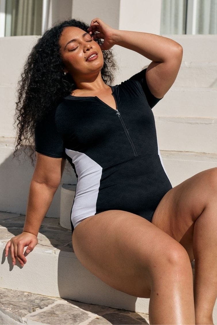 Close up image of model wearing a zip front detail one piece in black and white textured print