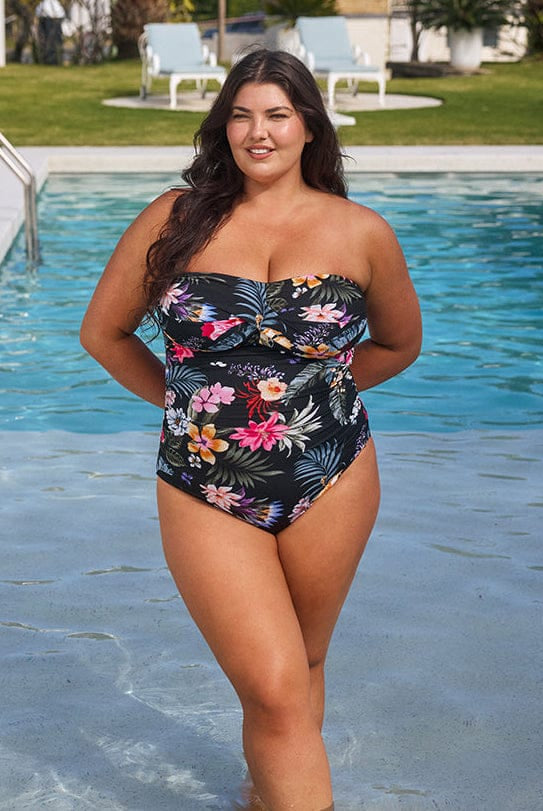 Woman in a floral swimsuit standing by a pool with greenery in the background