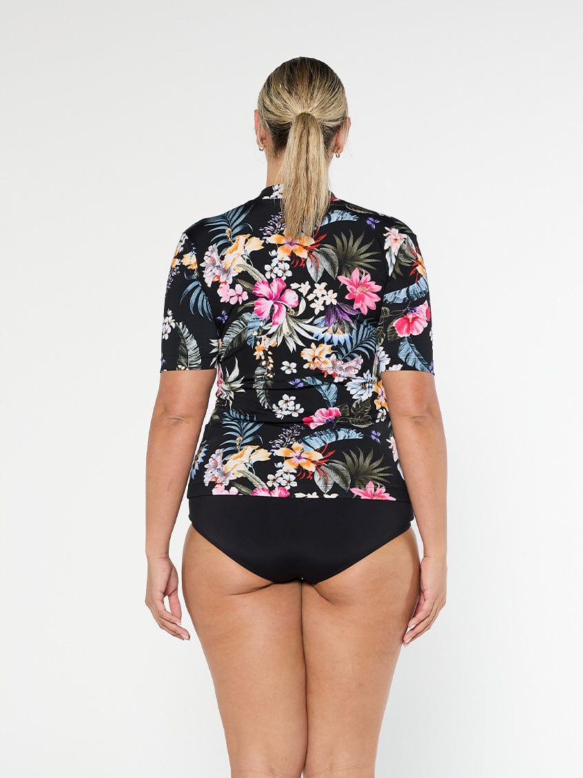 Blonde model shows back of short sleeve rash vest in chlorine resistant black floral fabric