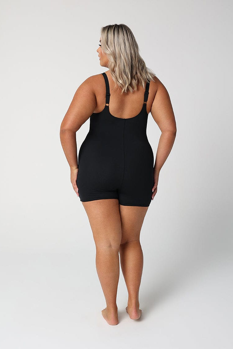 back of lady standing in front of a white wall wearing a black boyleg one piece