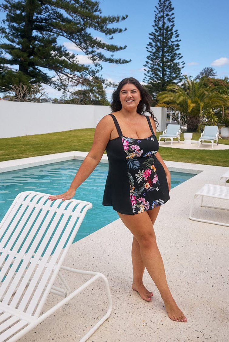 Woman in a floral dress standing by a pool with trees and chairs in the background