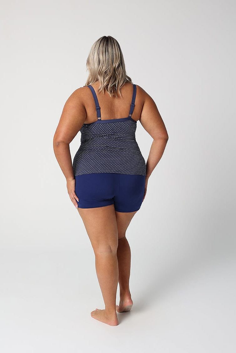 Person wearing a navy blue swimsuit with a white patterned top on a white background
