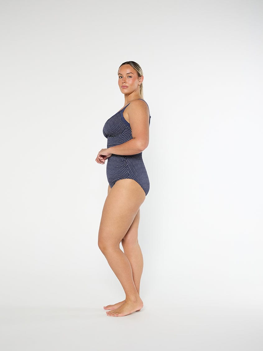 Woman wearing a navy polka dot swimsuit on a white background