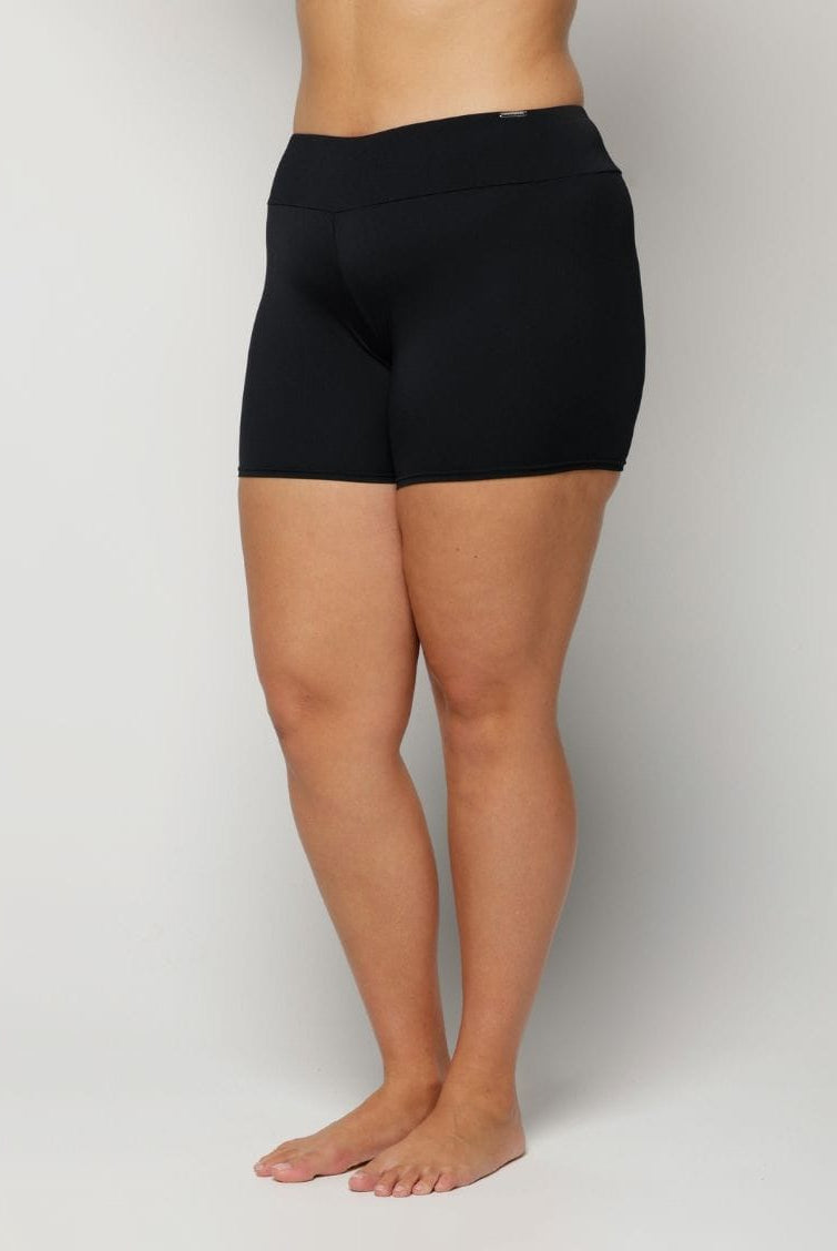 Woman wearing black swim shorts on a plain background