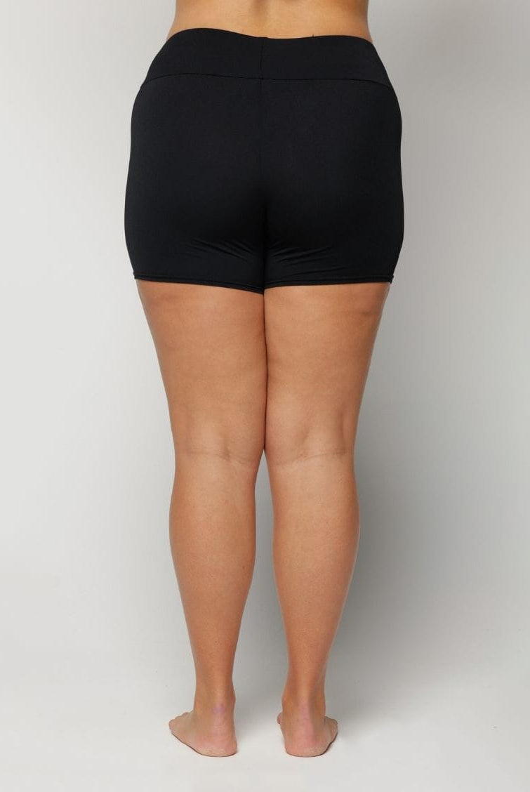 Woman wearing black swim shorts on a plain background