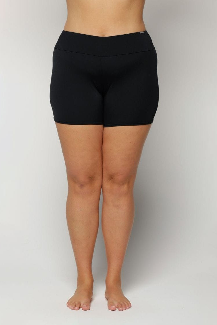 Woman wearing black swim shorts on a plain background