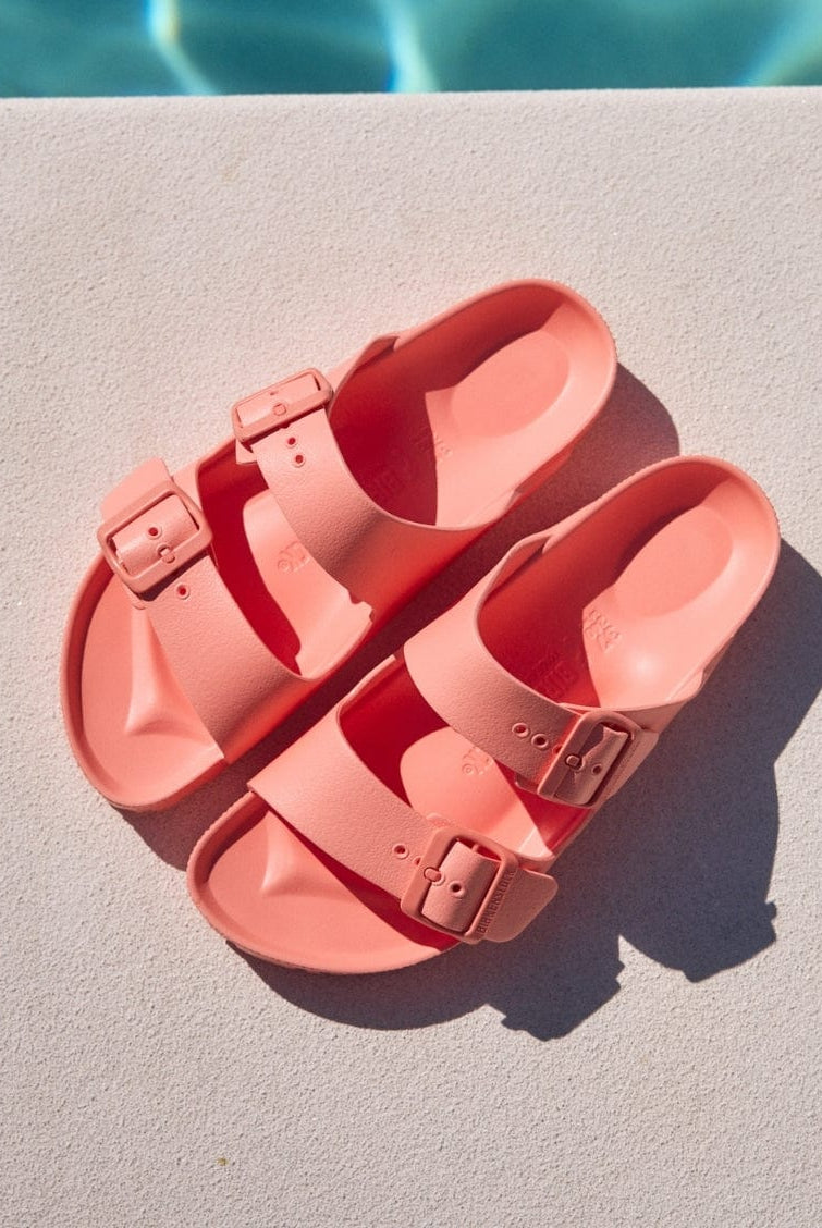Pair of pink sandals on a light surface with a pool in the background