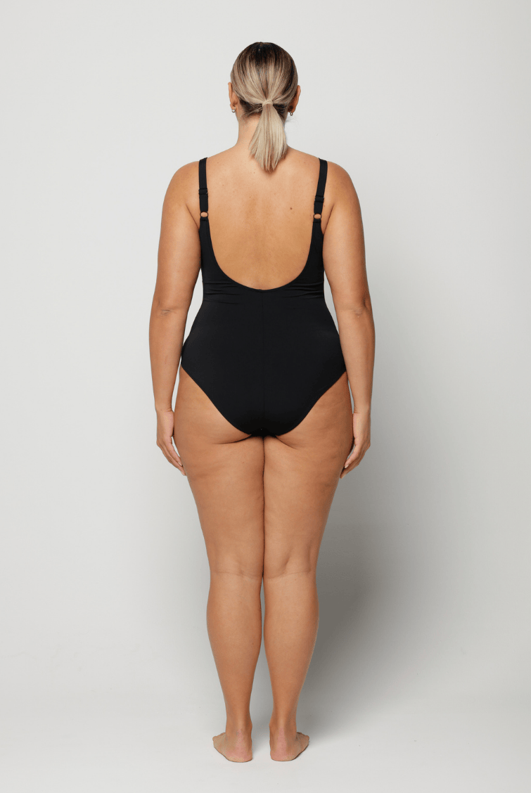Woman wearing a black criss cross swimsuit with blue floral patterns and scoop back
