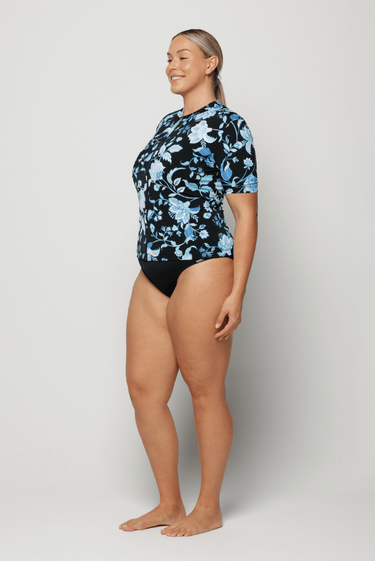 Woman wearing a black floral short sleeve rash vest on a white background
