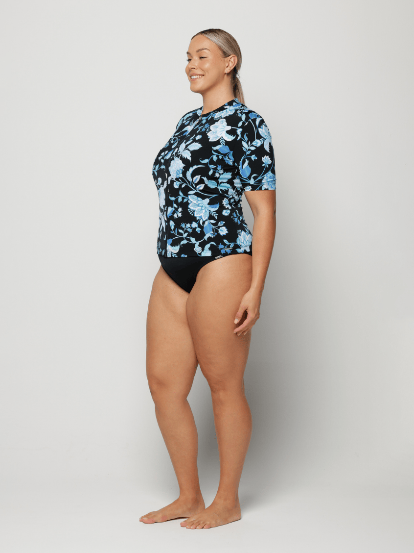 Woman wearing a black floral short sleeve rash vest on a white background