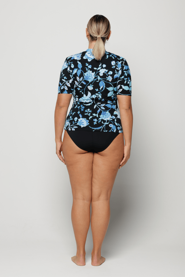 Person wearing a black floral rash guard and black swimsuit bottoms on a white background