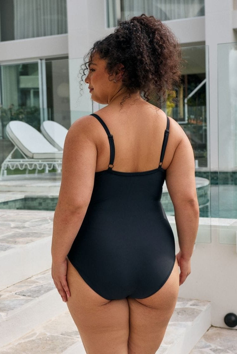 Back of model wearing a classic black one piece with adjustable straps in metallic black with criss cross detail