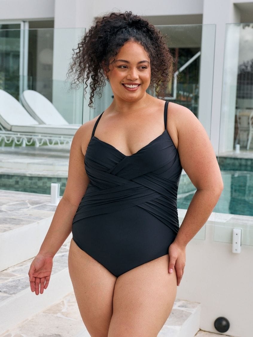 Brunette model wearing a black classic one piece with criss cross detail in metallic fabric