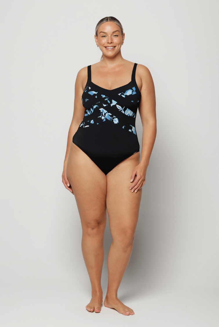 Woman wearing a black criss cross swimsuit with blue floral patterns on a white background