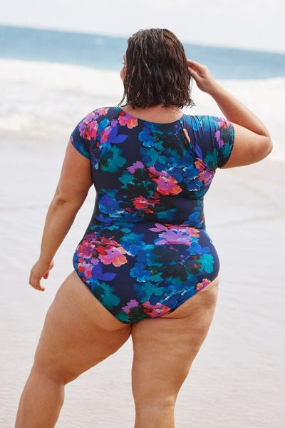 Back of model wearing flattering plus size swimsuit with cap sleeves in purple and navy floral print