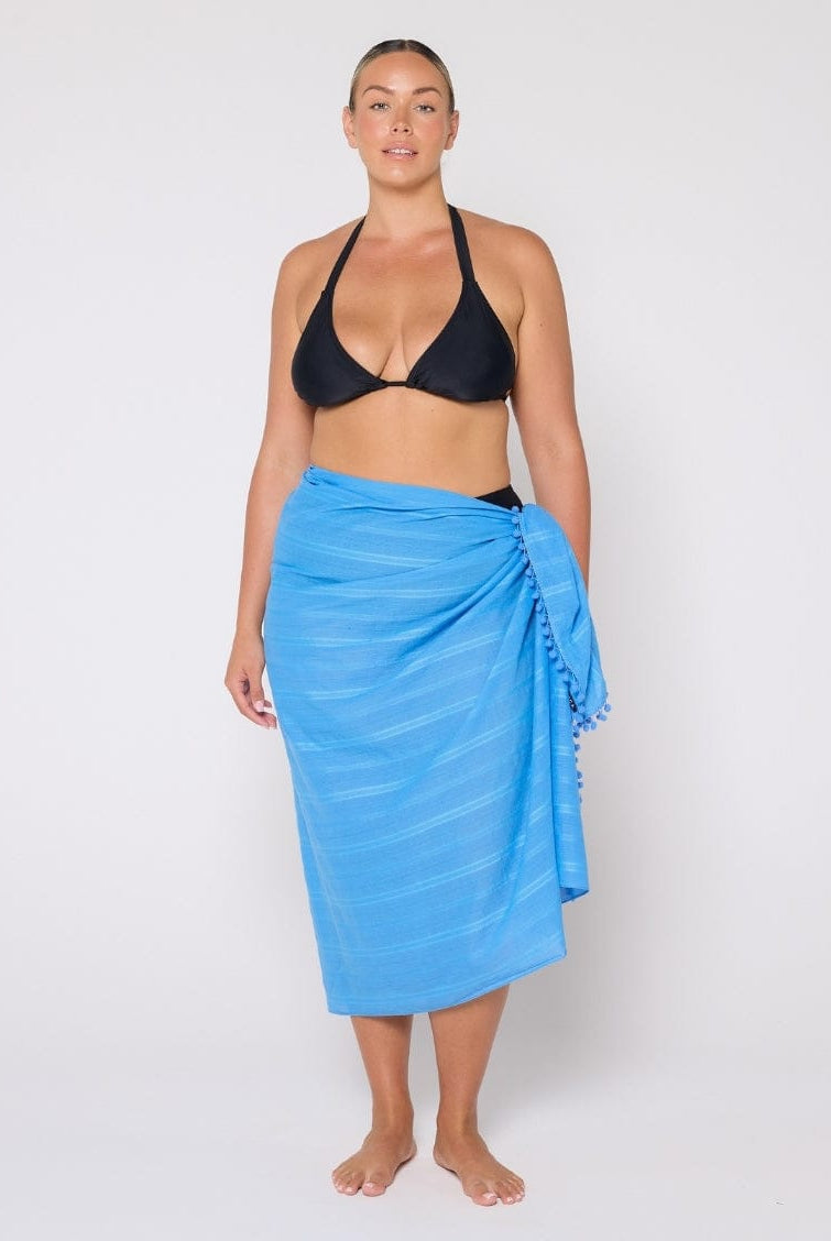 Woman wearing a black bikini top and blue sarong on a white background