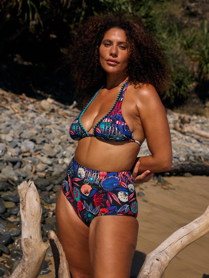 Model on beach wearing a curvy triangle bikini top with embroidered detail and multicoloured print