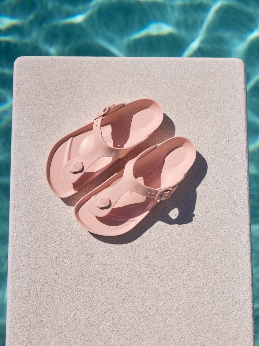 Pair of pink sandals on a diving board by a pool
