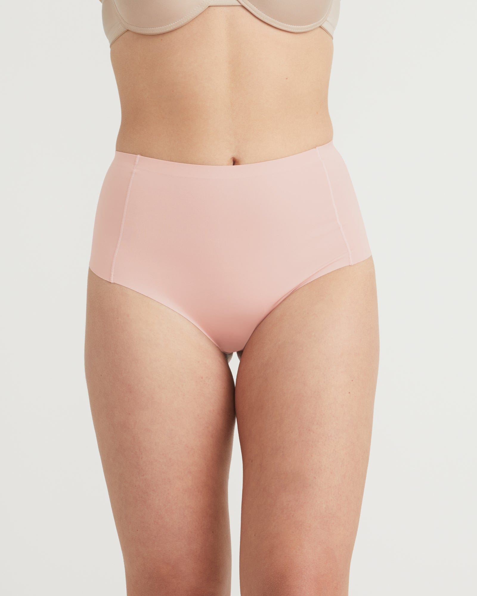 Person wearing a light pink high-waisted underwear on a plain background