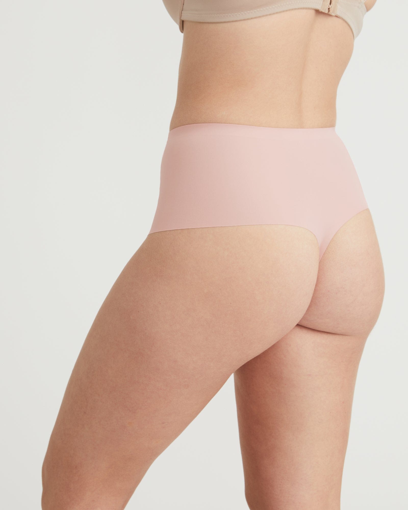 Person wearing a light pink high-waisted shapewear garment on a plain background