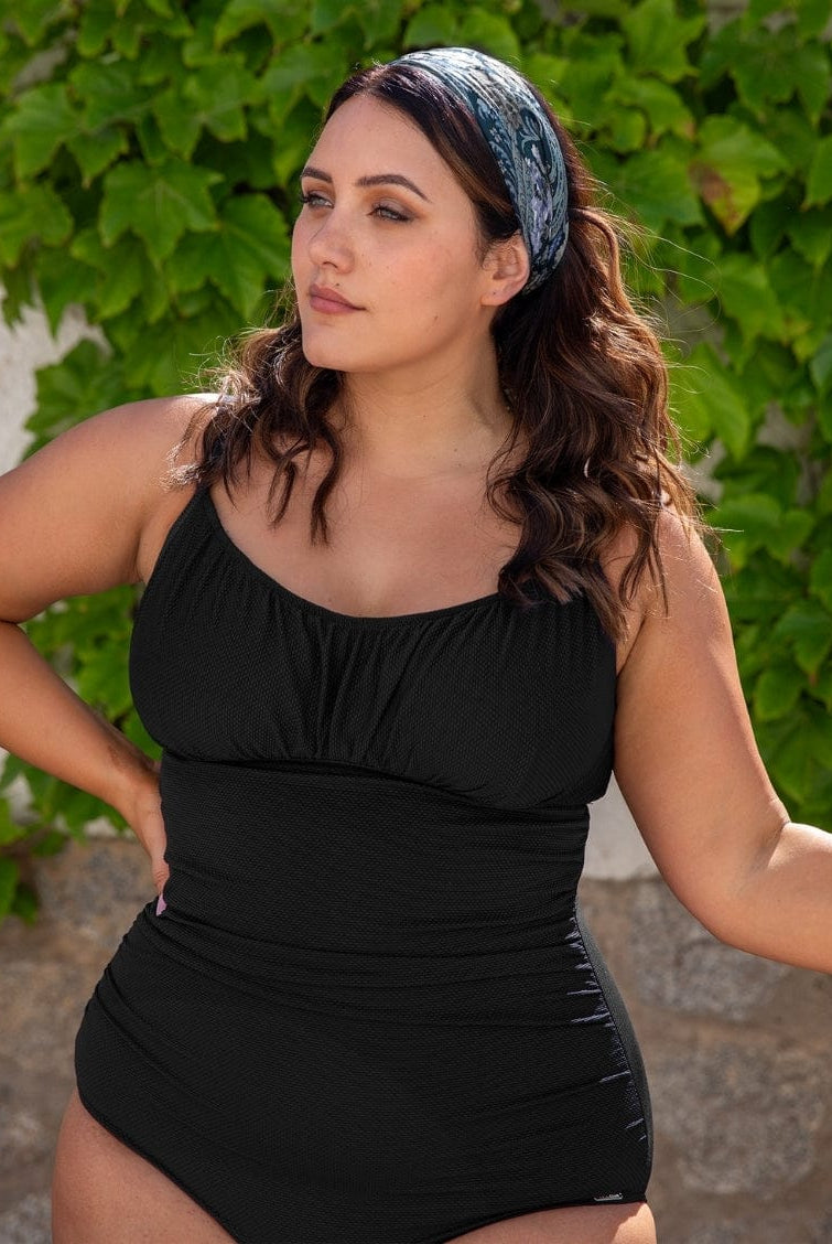 Woman wearing a black swimsuit with greenery in the background