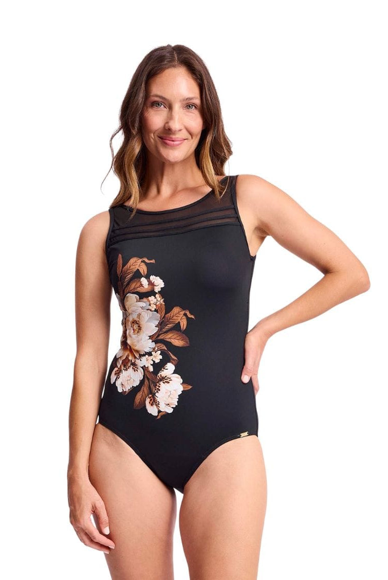 A woman modeling a black one-piece swimsuit with a floral print on the left side, featuring sheer mesh shoulder straps, set against a plain white background.
