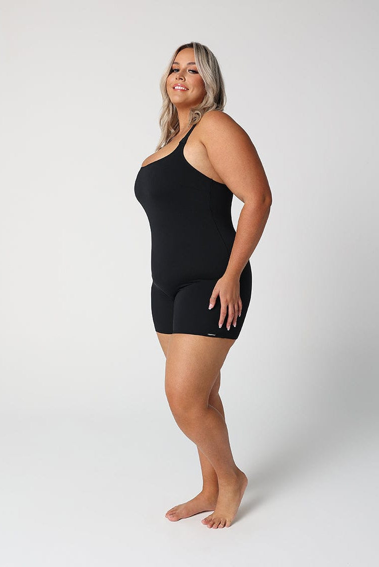 women standing side on in front of a white wall wearing a black boyleg one piece