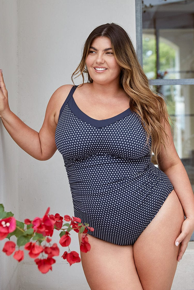 Woman wearing a navy blue polka dot swimsuit standing outdoors with a blurred background