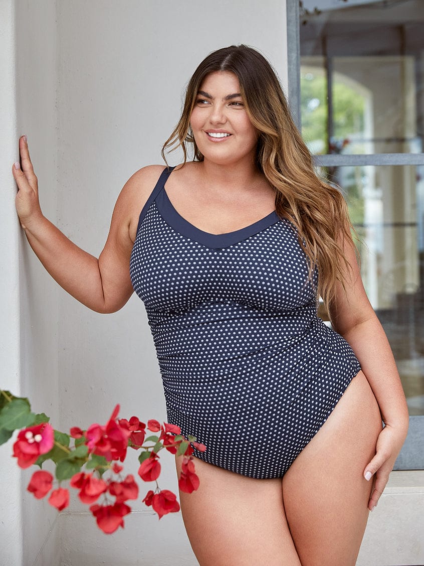 Woman wearing a navy blue polka dot swimsuit standing outdoors with a blurred background